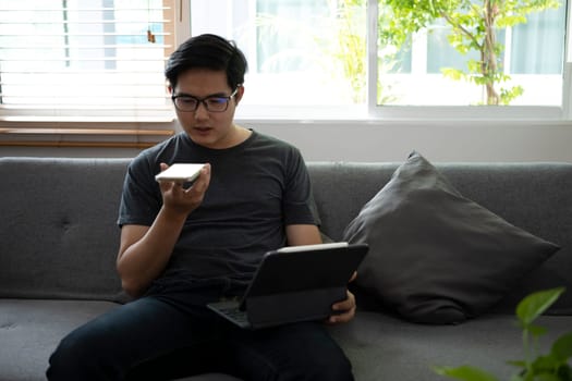 Young man holding smart phone and working with computer tablet in living room.
