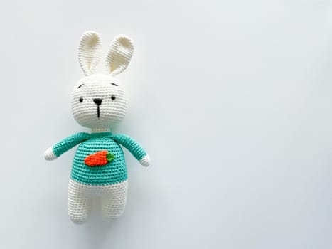 Soft white crochet bunny. on a white background. Handmade children's toy. Large knitted plush rabbit with a carrot on his chest. happy childhood concept