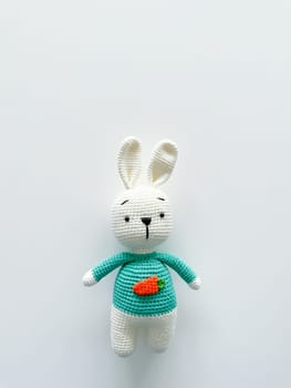 Soft white crochet bunny. on a white background. Handmade children's toy. Large knitted plush rabbit with a carrot on his chest. happy childhood concept