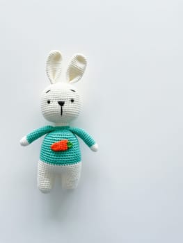 Soft white crochet bunny. on a white background. Handmade children's toy. Large knitted plush rabbit with a carrot on his chest. happy childhood concept