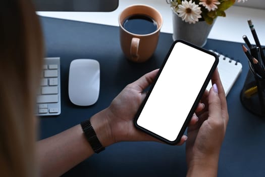 Young woman sitting at her workplace and using smart phone.