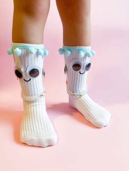 Baby socks with eyes and a smile on a pink background. Cute funny socks with eyes and decorations on the feet of a child.