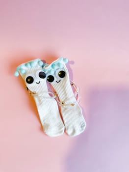 Baby socks with eyes and a smile on a pink background. Cute funny socks with eyes and decorations on the feet of a child.