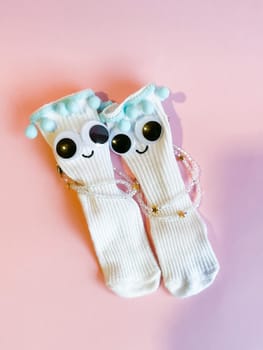 Baby socks with eyes and a smile on a pink background. Cute funny socks with eyes and decorations on the feet of a child.