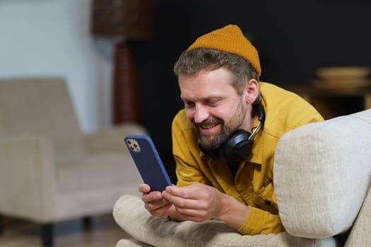 Man in casual spending his leisure time home on sofa, engrossed in phone. He texting someone using messaging app, indicating active communication through digital means. High quality photo