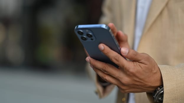 Cropped image of businessman texting messages, chatting in social on smartphone while standing outdoor.