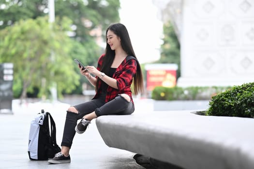 Young Asian woman sitting in city park and using smart phone.