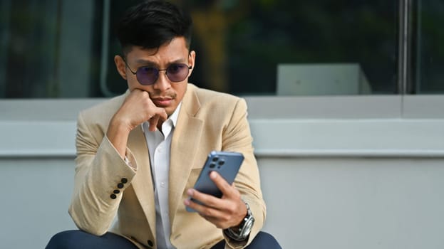 Young businessman in formalwear using smartphone in front of business center. Business, technology and lifestyle.