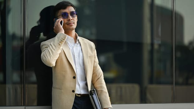 Elegant young businessman wearing stylish suit having phone conversation in a urban town.