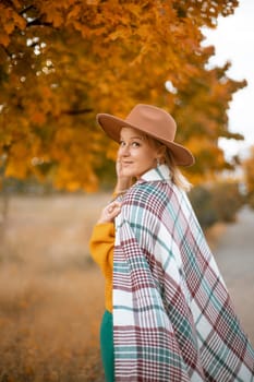 autumn woman in a green dress, brown hat, plaid, against the background of an autumn tree.