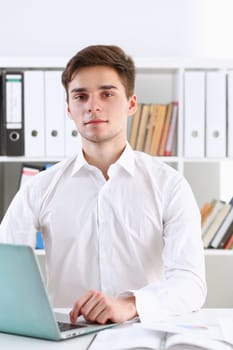 Young handsome businessman portrait in office sitting at table and working information laptop computer