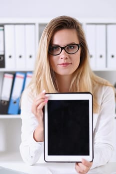 Beautiful businesswoman wearing glasses portrait at the office holding a tablet in hand sitting at the table smiling and looking at the camera teacher expresses success checking the test papers.