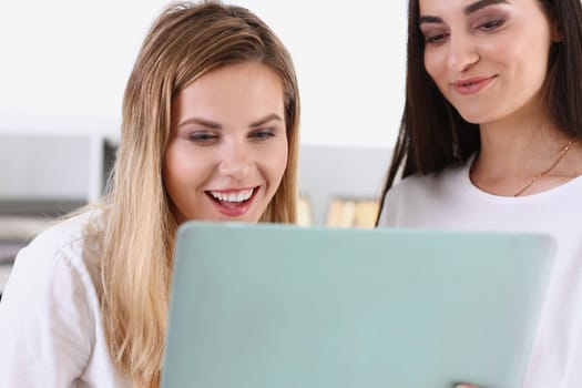 Two pretty women watching a funny video on a laptop laugh and smiling