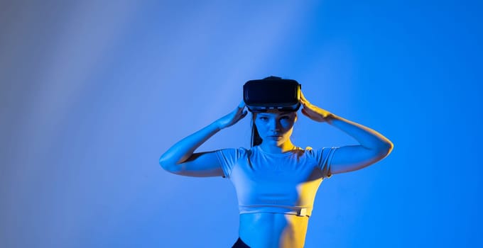 Young woman wearing virtual reality goggles and speasing with a friends in the metaverse. Famale in a black top exploring virtual reality video games in a studio