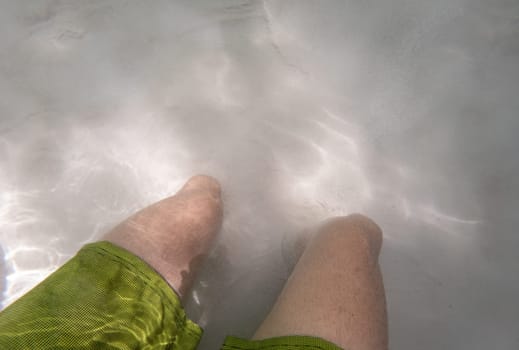 A pair of legs in a bathing suit sink into the sand of a fervedouro in Jalapao, disappearing underwater.