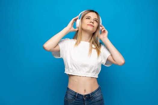 Young blonde woman with headphones listening music .Music teenager girl dancing against isolated blue background