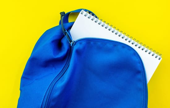 School backpack and notebook on a yellow background. School blue backpack with a notepad inside on a yellow background.