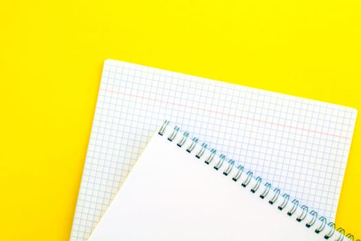 White notepad and notebook in a cage on a yellow background. School white notepad and notebook in a cage on a yellow background.