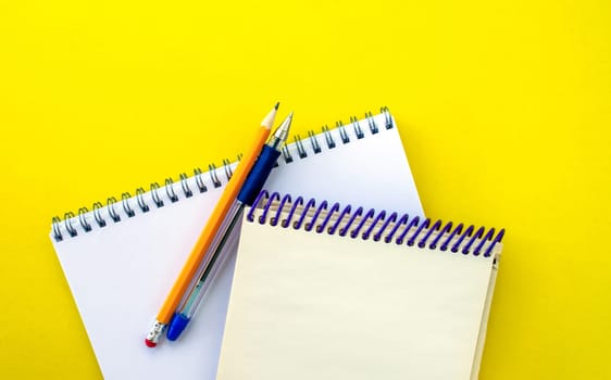 White and beige notepads, pen and pencil on a yellow background. School white and beige notebooks, pen and pencil on a yellow background.