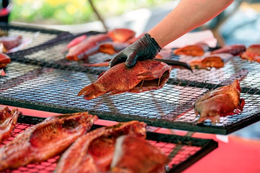 The process of smoking sea bass. A woman in a fish smoking factory lays out sea bass for smoking on a grill. The concept of the fishing industry. High quality photo