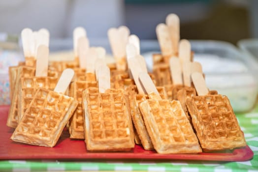 Belgian waffles on a wooden stick covered with chocolate icing. Production and sale of fresh Belgian waffles in a pastry shop. High quality photo