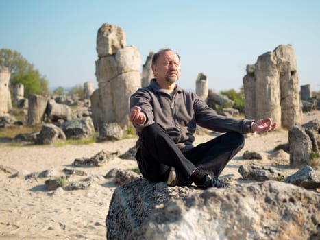 Outdoor Senior man meditating in lotus pose. Sunrise meditation in a magical place Stone Forest similar to Stonehenge, mindfulness concept