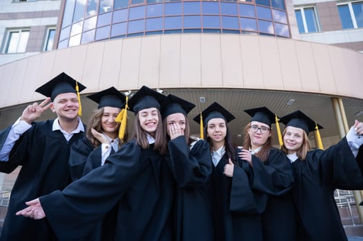 Happy students in graduate gown stand in a row against the backdrop of the university