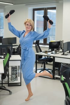 Caucasian business woman stands barefoot with shoes in her hands among the office