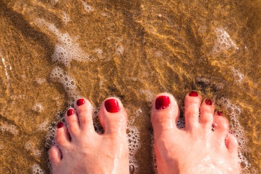 Woman's legs wear jeans with bare feet stand on sand at beach, hello summer.Girl bare foot relaxing in clear water