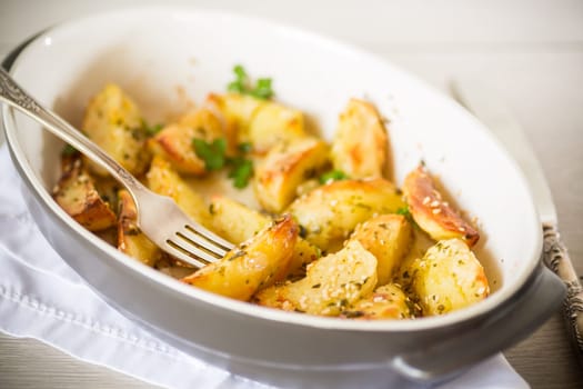 potatoes baked with sesame seeds, herbs and spices in the oven in a ceramic form.