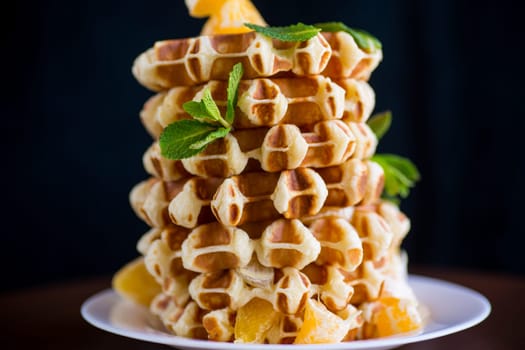 Cooked sweet Belgian waffles with oranges on a black background