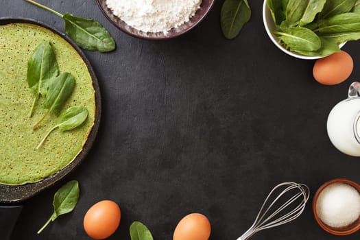 Spinach pancake in a pan on a black background with ingredients: eggs, spinach, milk, flour. Cooking. copy space