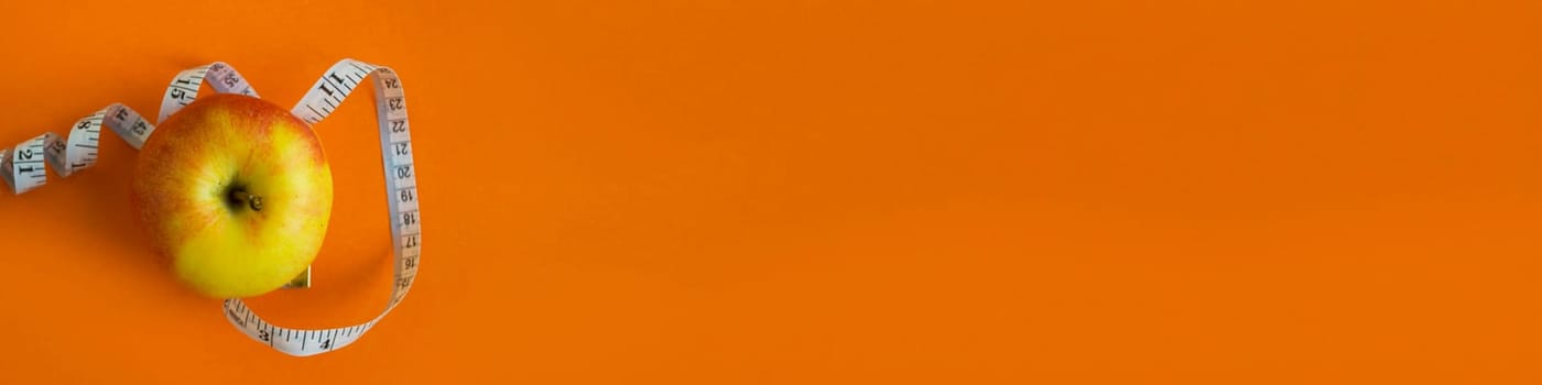 Banner. Apple and a centimeter tape on an orange background close-up.