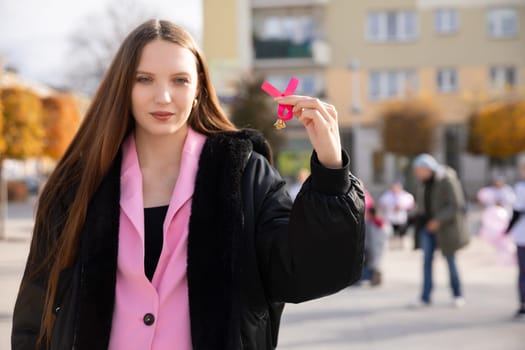 A young woman is holding a pink ribbon in solidarity with the essential prevention of breast examinations.