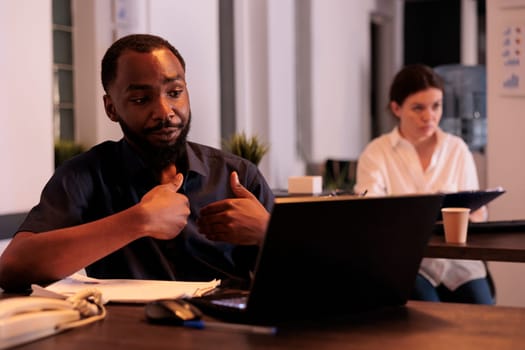 Employee discussing company report on videoconference with teamlead, corporate worker answering teleconference call in office at night. African american man remote conversation with client