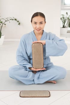 Asian woman sitting in lotus position on yoga mat and holding sadhu boards