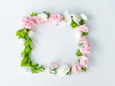 Square frame of pink and white carnations, green leaves, gypsophila on a white background. Flat lay, top view. Spring background. Suitable for wedding, cards and invitations