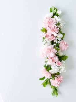 Beautiful delicate blooming floral frame of pink carnations, gypsophila, buds, leaves on a white background, top view, flat lay