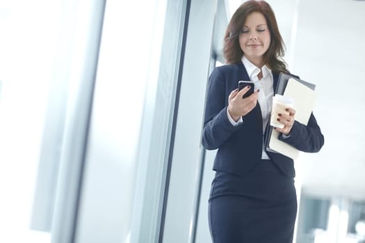 Happy businesswoman using her phone and drinking a coffee at work. One female businessperson browsing online using social media on a break in an office. Business professional sending a text message.
