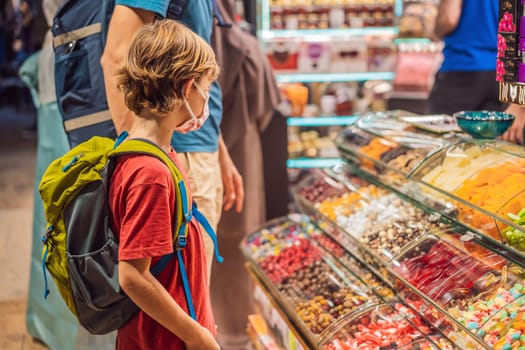 The boy looks at the counter with Turkish sweets. Traditional oriental sweet pastry cookies, nuts, dried fruits, pastilles, marmalade, Turkish desert with sugar, honey and pistachio, in display at a street food market.