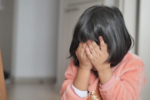 a upset child girl cover her face with hand .