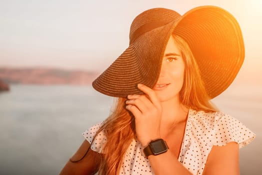 Portrait of happy young woman wearing summer black hat with large brim at beach on sunset. Closeup face of attractive girl with black straw hat. Happy young woman smiling and looking at camera at sea