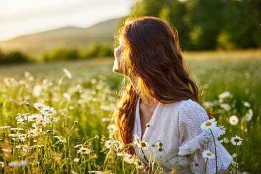 portrait of a beautiful, red-haired girl sitting in a chamomile field and looking at the sunset. High quality photo