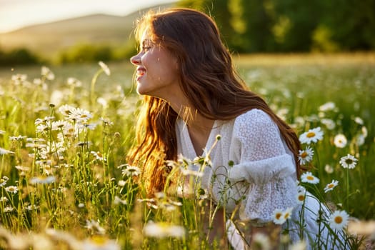 portrait of a beautiful, red-haired girl sitting in a chamomile field and looking at the sunset. High quality photo