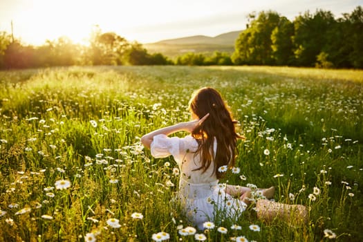 a red-haired woman in a light dress sits in a chamomile field at sunset and admires the passing day. High quality photo