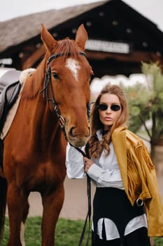 Stylish girl with glasses stands next to a horse on the street.