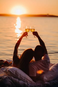 Silhouettes of a happy couple raising glasses on a summer evening near the sea at sunset.