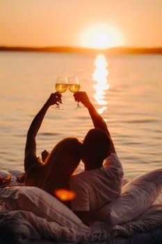 Silhouettes of a happy couple raising glasses on a summer evening near the sea at sunset.