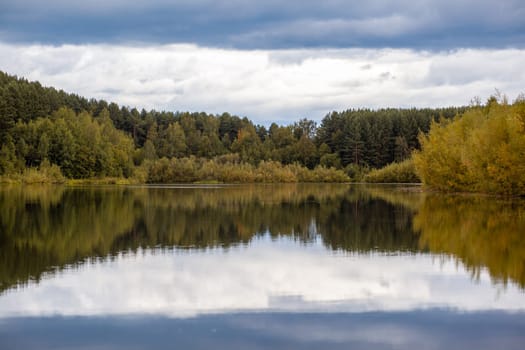 Colorful foliage tree reflections in calm pond water on a beautiful autumn day. A quiet and beautiful place to relax.