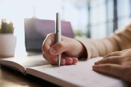 Businessman writes with a pen in diary in a sunny office, business and education concept. Close up